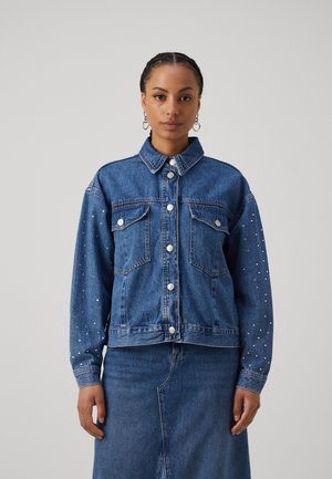 Giacca di jeans con colletto, bottoni argentati, due tasche sul petto e dettagli in borchie sottili sulle maniche. Colore blu classico e vestibilità standard.
