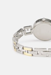 Ezüst és arany színű rozsdamentes acél óra geometrikus láncbracelettel, kerek tokkal és textúrázott hátlappal. Oldalán koronával rendelkezik.