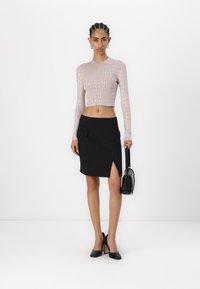 Lys rosa crop-longermet topp med gjentatt logo-mønster, parret med et svart omslagsskjørt med sideluk og lomme; svart håndveske.
