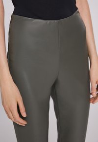 Aansluitende donkergroene broek van glad nepleer, met een hoge taille en een slanke silhouet, met een subtiele glans.