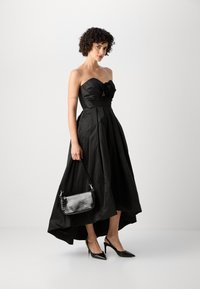 Juoda strapless suknelė su tekstūruotu liemeniu, gėlių detale ir pilna sijonu. Pora su juoda blizgia rankine ir smailiais kulnais.