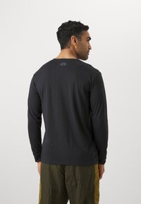 Schwarzes Langarmshirt mit rundem Halsausschnitt, das auf der Rückseite ein dezentes Logo trägt. Der Stoff wirkt glatt und leicht.