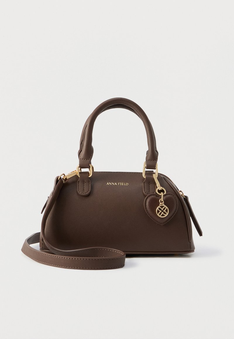 Hnedá syntetická kabelka zaobleného tvaru, s dvoma hornými rúčkami a odnímateľným ramenným popruhom. Obsahuje zlaté kovanie a prívesok v tvare srdca.
