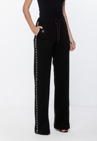 Czarne szerokie spodnie dresowe z elastycznym pasem na sznurek, bocznymi kieszeniami i kontrastującymi paskami po bokach z wzorem serc.