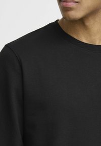 Zwarte katoenen sweatshirt met een ronde hals en ribgebreide manchetten, met een gladde textuur en minimalistisch ontwerp. Geen patronen of grafische elementen aanwezig.