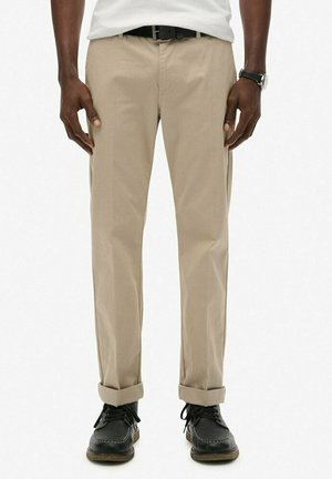Beige katoenen chino's met rechte pijpen, opgerolde manchetten en zijzakken, gecombineerd met zwarte leren schoenen en een riem.