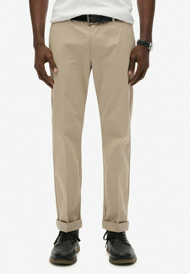 Chinos de algodón beige con piernas rectas, puños enrollados y bolsillos laterales, combinados con zapatos de cuero negro y un cinturón.