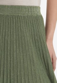 Grön plisserad kjol i strukturerad tyg med metalltrådar, med bred elastisk midja och vertikala plisseringar för extra detalj.