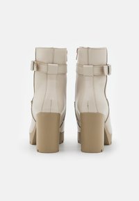 Stivali con tacco beige realizzati in pelle liscia, con zip laterale, cinturino regolabile con fibbia e design con tacco spesso.