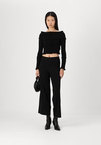 Crni rebrasti crop top s dizajnom bez naramenica, uparen s crnim širokim hlačama viskog struka. Dodaci uključuju malu crnu torbicu.