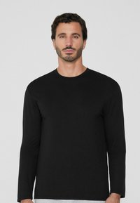 Schwarzes Langarm-T-Shirt aus Baumwolle. Verfügt über einen runden Ausschnitt und eine taillierte Passform. Glatte Textur und keine sichtbaren Muster oder Akzente.