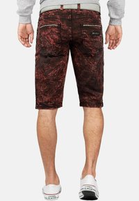 Shorts en denim rouge et noir avec une finition usée, accents de clous sur les côtés et matériel métallique sur les poches arrière.