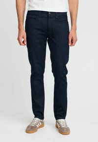 Mörk denimjeans med slim fit, standard femficksdesign och knäppning. Bärs med ljusa sneakers.