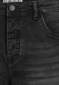 Black denim jeans with a textured finish, featuring a button closure, five-pocket design, and a branded label on the waistband.