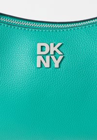 Türkiissinine käsikott, millel on tekstureeritud nahkpind, hõbedane "DKNY" logo ja peal oleva luku sulgemine.