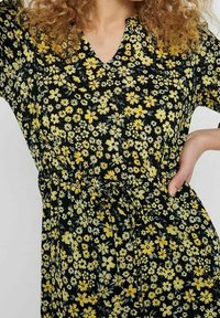 Vestido negro con un patrón floral en amarillo y blanco. Escote en V, mangas cortas y una cinturilla ajustable para un mejor ajuste.