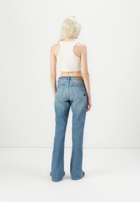 Jeans din denim albastru deschis, evazați, cu talie înaltă, având un petic din piele pe spate și o ușoară decolorare. Top alb scurt, tip s tank.