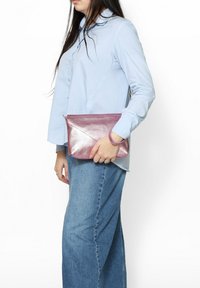 Clutch in pelle metallizzata rosa con design geometrico, dotato di chiusura a zip e tracolla, tenuto contro una camicia blu e jeans di jeans.