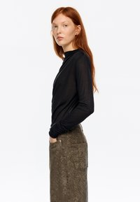 Czarna bluzka z długim rękawem i wysokim kołnierzem, zestawiona z oliwkowo-zieloną teksturowaną spódnicą z kieszenią i subtelnym wzorem.