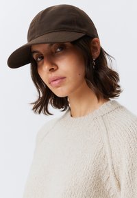 Καφέ βαμβακερό καπέλο μπέιζμπολ με καμπύλη γείσο, που διαθέτει ορατές ραφές και έναν υφασμάτινο, υφασμάτινο μπεζ πουλόβερ στο φόντο.