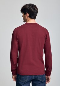 Bordeaux lange mouwen shirt met ronde hals, gemaakt van een katoenmix, met een gladde textuur en een casual ontwerp, gecombineerd met blauwe jeans.