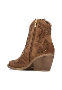 Stivale alla caviglia in suede marrone con chiusura a zip, borchie decorative dorate, design curvo e tacco medio a blocco. Pannelli laterali texturizzati.