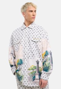 Witte shirt met herhaald logo-patroon; heeft kleurrijke geschilderde taferelen van bomen en colommen op de mouwen; knoopsluiting, twee voorkeizen.