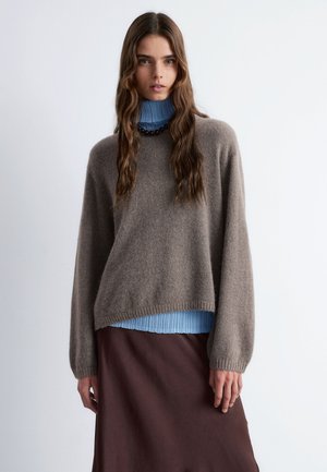 Brown knitted sweater with a relaxed fit, layered over a light blue ribbed turtleneck, paired with a dark brown skirt.