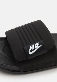 Black slide sandal made of soft material with a padded strap. Features a textured sole and a white Nike logo on the strap.