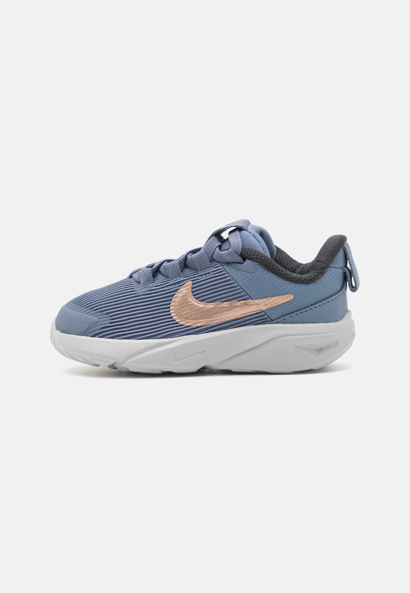Baskets Nike avec un matériau bleu nervuré, des accents en or rose, un talon gris et une semelle blanche, conçues pour le confort et le soutien.