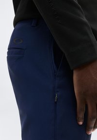 Κοντινό πλάνο ενός ατόμου που φοράει ναυτικά μπλε παντελόνια με τσέπη με φερμουάρ και μαύρο τοπ, δείχνοντας τις λεπτομέρειες της πλαϊνής και πίσω τσέπης.