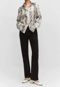 Langärmliges Hemd mit Knöpfen in Schlangenprintmuster, schwarz und weiß, kombiniert mit schwarzen Jeans und cremefarbenen Blockabsatzschuhen.