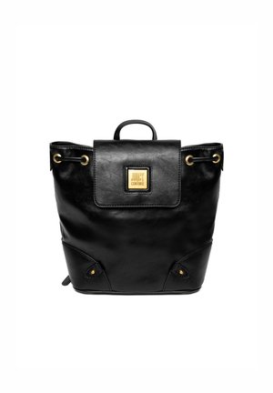 Sac à dos en cuir noir avec une fermeture à rabat, des accents dorés et une petite poignée supérieure. Il présente des coins arrondis et des rivets décoratifs sur les côtés.