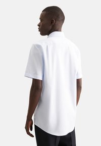 Camicia a maniche corte di colore azzurro chiaro, realizzata in tessuto liscio. Presenta un colletto classico e un orlo arrotondato, con cuciture pulite e senza decorazioni visibili.