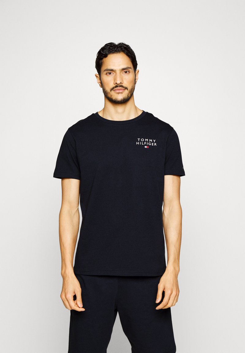 Zwarte katoenen t-shirt met korte mouwen, ronde halslijn, bevat een klein wit "TOMMY HILFIGER" logo aan de bovenste linkerzijde.