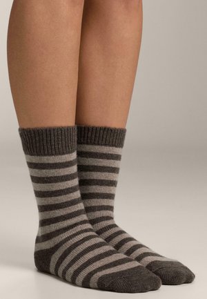 Benen met halflange geribbelde sokken met donker- en lichtgrijze horizontale strepen tegen een effen achtergrond.