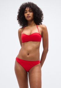 Σετ κόκκινου μπικίνι με μπαντό τοπ με στήριξη και λεπτές τιράντες, και ταιριαστά σλιπ με χαμηλή μέση, κατασκευασμένα από λείο, ελαστικό ύφασμα.