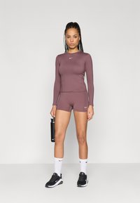 Športový outfit so priliehavým dlhým rukávom a zodpovedajúcimi šortkami v tlmenom odtieni marhuľovej farby, vyrobený z hladkej tkaniny s akcentami loga Nike.