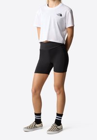 Vit kortärmad t-shirt med svart logotyp, ihopparad med svarta träningsshorts. Svart och vit rutmönstrade slip-on skor och svarta randiga strumpor.