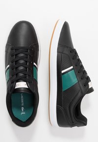 Zapatillas negras con un acabado de cuero suave, acentos en azul verdoso y blanco, paneles laterales perforados y una suela de goma texturizada.