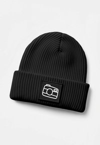 Black ribbed beanie with a folded cuff, featuring a white camera graphic on a square patch. Textured knit material.