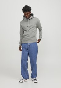 Gray hoodie with a kangaroo pocket, drawstring hood, and ribbed cuffs, paired with loose blue denim jeans and black-and-white sneakers.