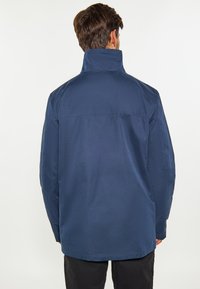 Marineblauwe jas met een hoge kraag, lange mouwen en een relaxte pasvorm. Glad textuur, minimalistisch ontwerp en geen zichtbare hardwaredetails.