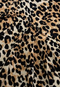 Tissu en imprimé léopard avec de grandes taches noires sur un fond beige, agr émenté de plis et de petits boutons qui mettent en valeur le design.
