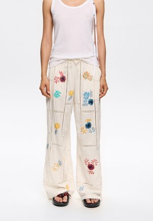 Lichte, crèmekleurige broek met bloemenborduursels in blauw, geel en rood, met een koord in de taille en wijde benen.