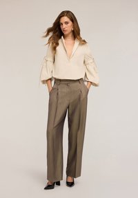 Beige bluse med dyb V-udskæring, puffærmer og bindebånd; parret med brune stribede vide bukser. Sorte lakpumps fuldender outfittet.