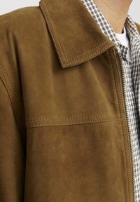 Brown suede jacket featuring a large collar, stitched detailing, and a zip closure, layered over a checkered shirt.