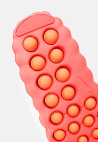 Εξωτερική σόλα παπουτσιού Nike από ροζ καουτσούκ με ανυψωμένα πορτοκαλί κυκλικά στοιχεία. Επιφάνεια με υφή για καλύτερο κράτημα, με κυματιστό άκρο και λεπτομέρεια λογότυπου.