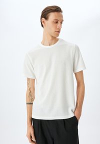 Vit kortärmad t-shirt med ett texturerat mönster och rund halsringning. Har en avslappnad passform och är kombinerad med svarta byxor.