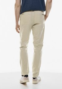 Béžové chinos vyrobené z bavlny se Slim fit, s dvěma zadními kapsami a prošíváním, v kombinaci s bílými teniskami.